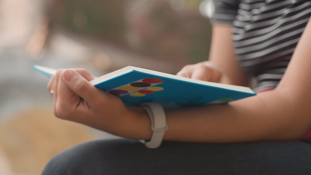 Closeup hands writing blue notebook urban, city bench setting with striped top, pen strokes and watch on wrist, evening soft light, shallow depth of field, commuter study routine, focused calm mood