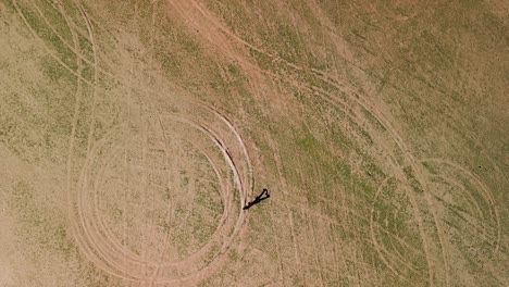 aerial drone shot of a girl walking over unusual ground formations in an arid, dry landscape with patches of sparse vegetation