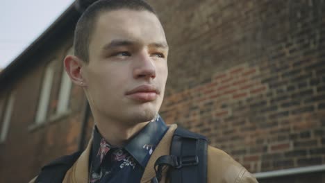 A-Young-Man-Standing-Outside-Looking-Around-With-Old-Brick-Building-Background---Low-Angle-Shot,-Slow-Motion