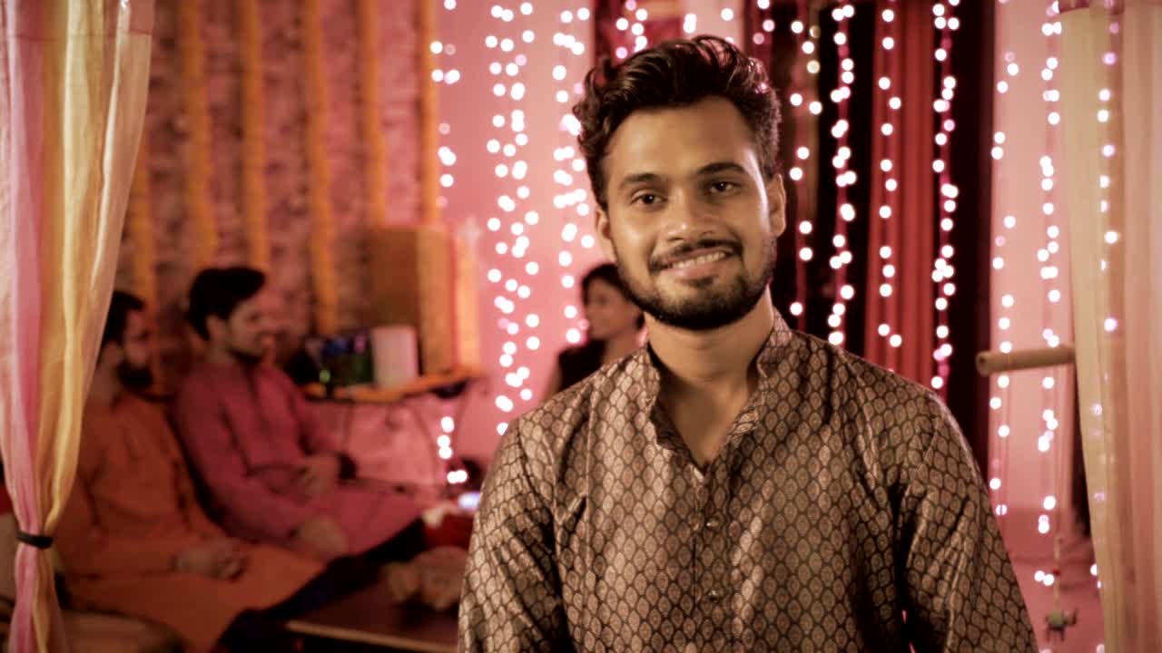 A male wearing Kurta smiling during Diwali festival while group of friends talking in the back