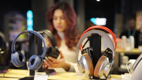 cheerful young woman buying new headphones in tech store department. high quality 4k footage