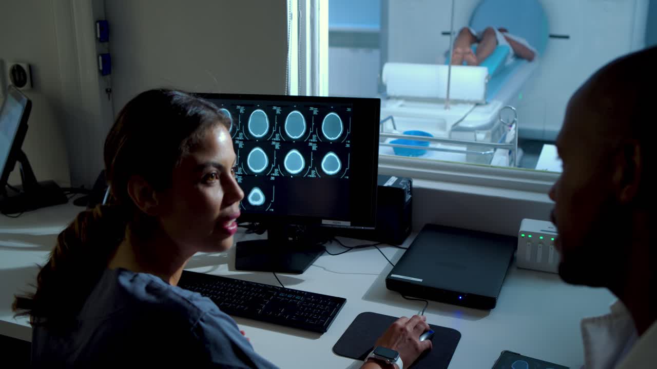 Scanner MRI che invia immagini, tecnico afroamericano e medico che esaminano le scansioni per la cura al monitor.