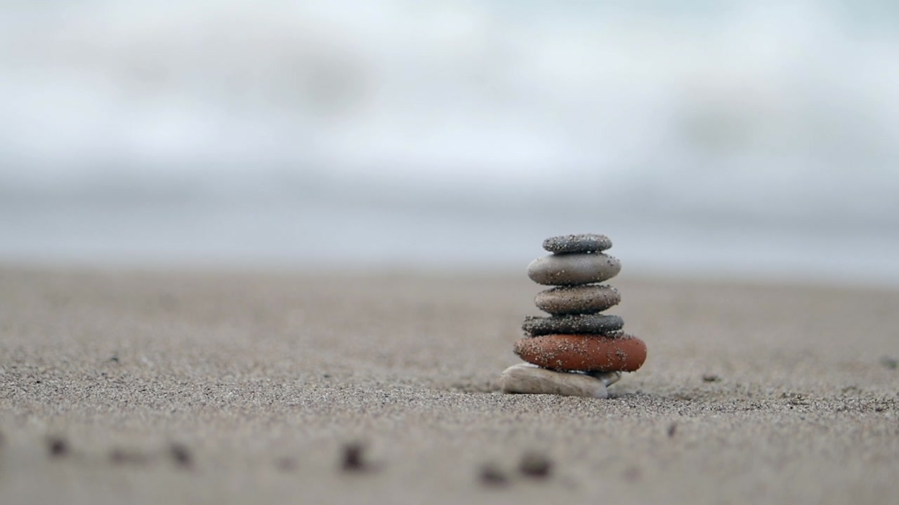 Ocean Wave Washing Over a Stack of Balanced Stones on a Sandy Beach