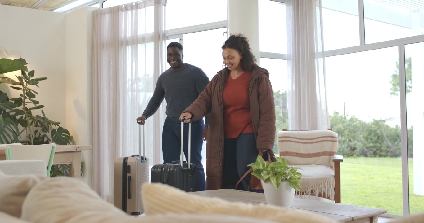 Couple afro-américain entrant par des portes vitrées, la femme en manteau marron tirant des valises et s'installant