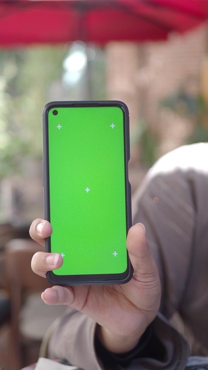 Mano che tiene uno smartphone con schermo verde e marcatori di tracciamento