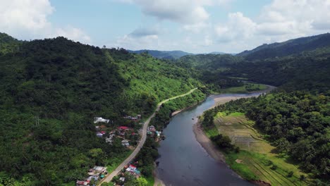 aerial dolly forward above tropical village and road way following river valley