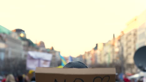 Cardboard-protest-sign-against-war-raised-above-rally-crowd,-close-up