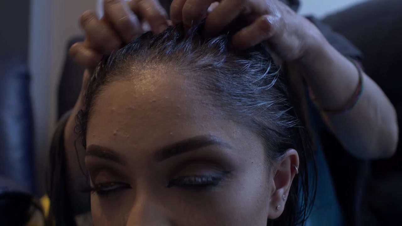Jovem mulher asiática recebendo massagem capilar enquanto está sentada. Close-up, plano fixo, ângulo baixo.