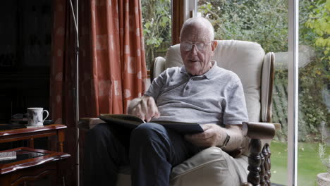 elderly man reading a book in an armchair at home