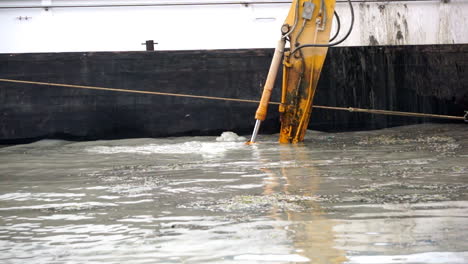 Shot-of-the-shovel-of-an-excavator-on-a-pontoon-next-to-a-ship,-deepening-a-canal