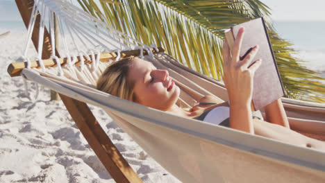 Mujer-Caucásica-Tumbada-En-Una-Hamaca-Y-Leyendo-Un-Libro-En-La-Playa