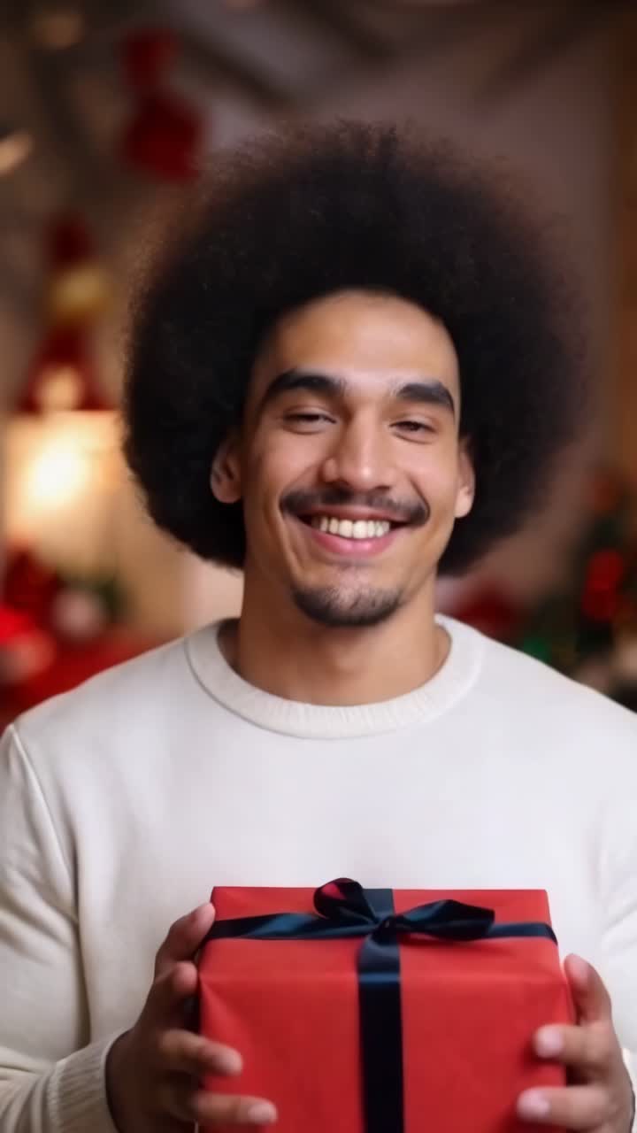 An afro man is holding a red box with a black ribbon. He is smiling. Christmas celebration