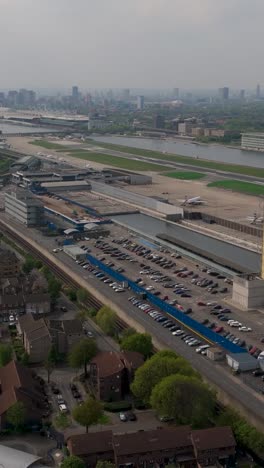 Vertical drone flying towards London City Airport terminal with planes and misty skyline