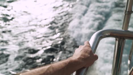 Man's-hand-holding-metal-bar-on-a-boat-sailing-in-the-ocean