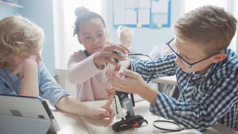 aula de robótica de escuela primaria: grupo diverso de niños brillantes construyendo y programando robots, hablando y trabajando en equipo. niños aprendiendo diseño de software e ingeniería robótica creativa