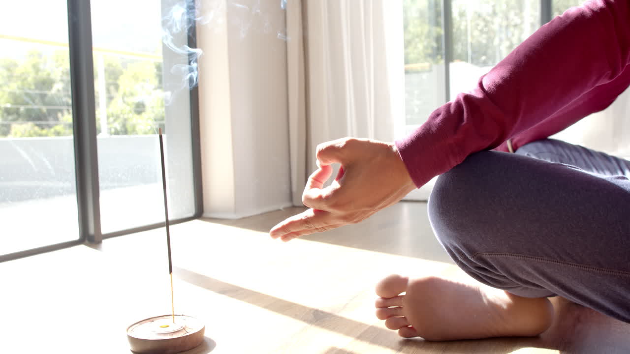 Meditating at home, man sitting cross-legged with incense burning nearby