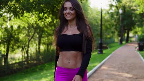 smiling brunette woman in short sport top walking in the park after intensive training. fit healthy sport woman exercising in