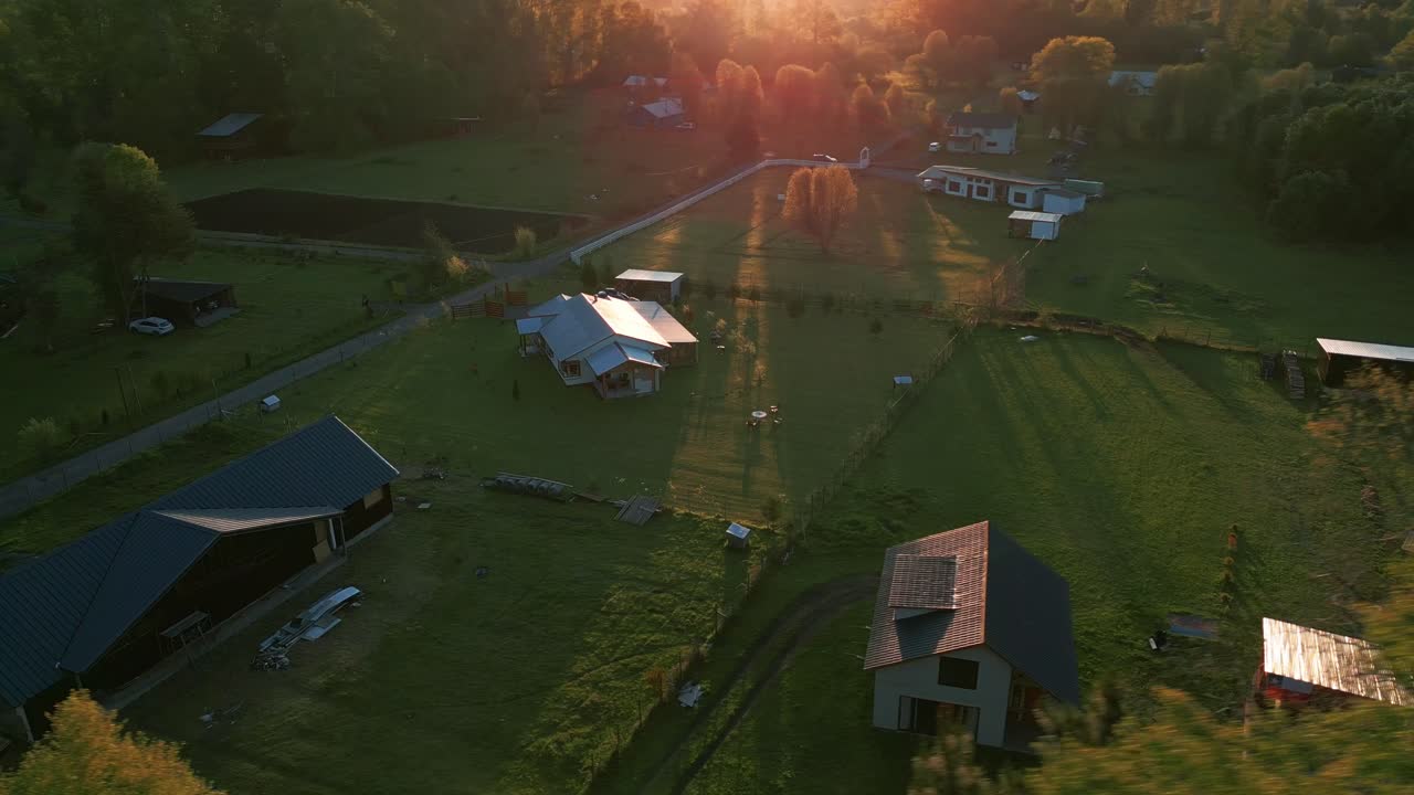 Luftbåren kreds af landhuse under solnedgang, med lange skygger, grønne områder og snoet vej, der fremhæver det fredfyldte landskab.