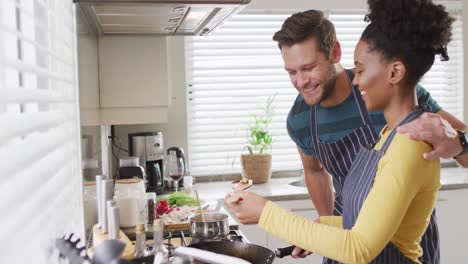 video de una feliz pareja diversa preparando una comida, probando un plato
