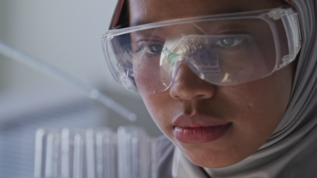 Female Laboratory Technician in Hijab Filling Test Tubes with Blue Liquid