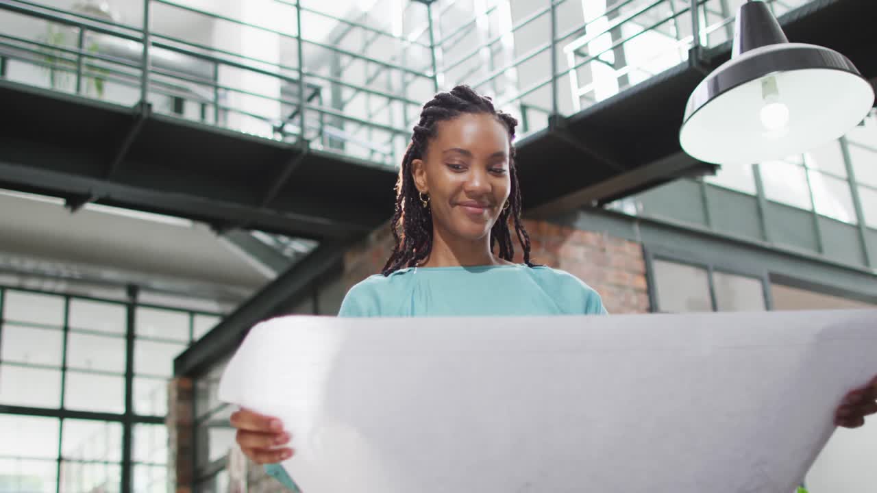 Happy african american female architect looking at architectural blueprints at office