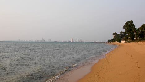 Schöne-Ruhige-Wellen-Entlang-Des-Strandes-Von-Bangsaray-In-Pattaya,-Thailand-Mit-Stadtgebäuden-Am-Horizont-Im-Hintergrund