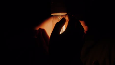 a man holds his hands around an electric light bulb