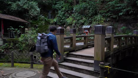 male hiker walking over bridge in beautiful temple inside dark forest