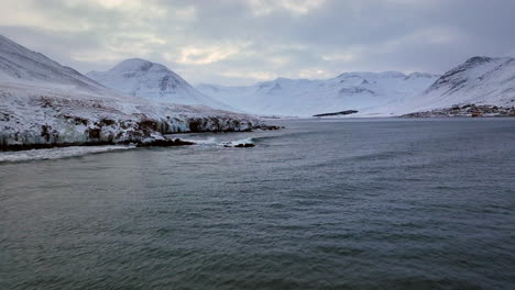 Waves-crash-against-the-rocks-in-a-bay-surrounded-by-high-snowy-mountains-in-Iceland