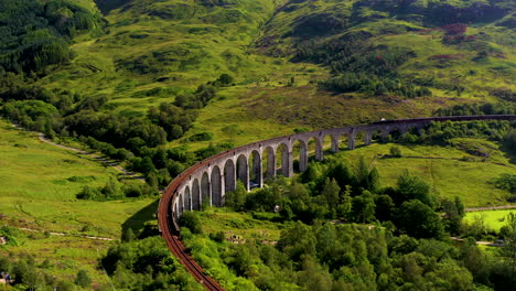 rotating drone shot of famous railroad bridge in the glenfinnan viaduct with train on the tracks