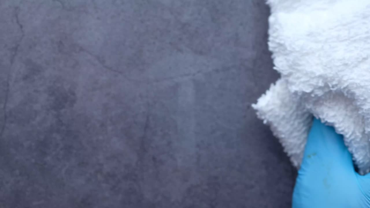 limpieza de una superficie gris con una toalla blanca y guantes azules