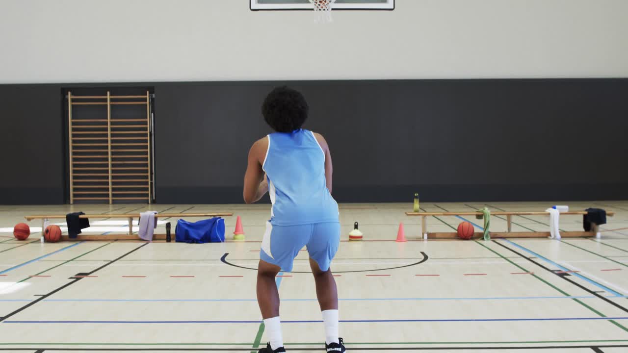 jugador de baloncesto afroamericano disparando pelota en el aro, entrenando en la cancha cubierta, cámara lenta