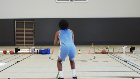 african american male basketball player shooting ball at hoop, training at indoor court, slow motion