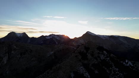 Panoramic-wide-aerial-as-sun-flare-spreads-across-mountain-peaks-of-Agrafa-Greece,-nature-backdrop