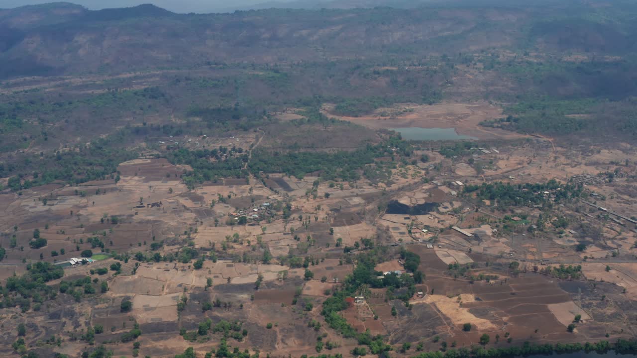 Un drone sale lentamente dal tortuoso fiume Amba, rivelando estese terre agricole aride, vegetazione rada, piccoli stagni, strade e colline distanti nella regione di Pali Raigad, Maharashtra.