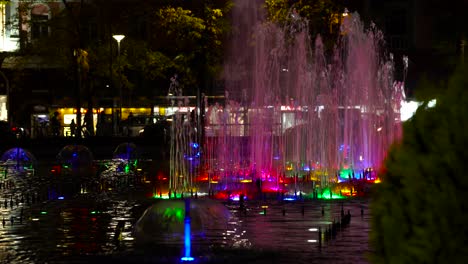 colorful water fountain at night with people and cars moving on background in tirana