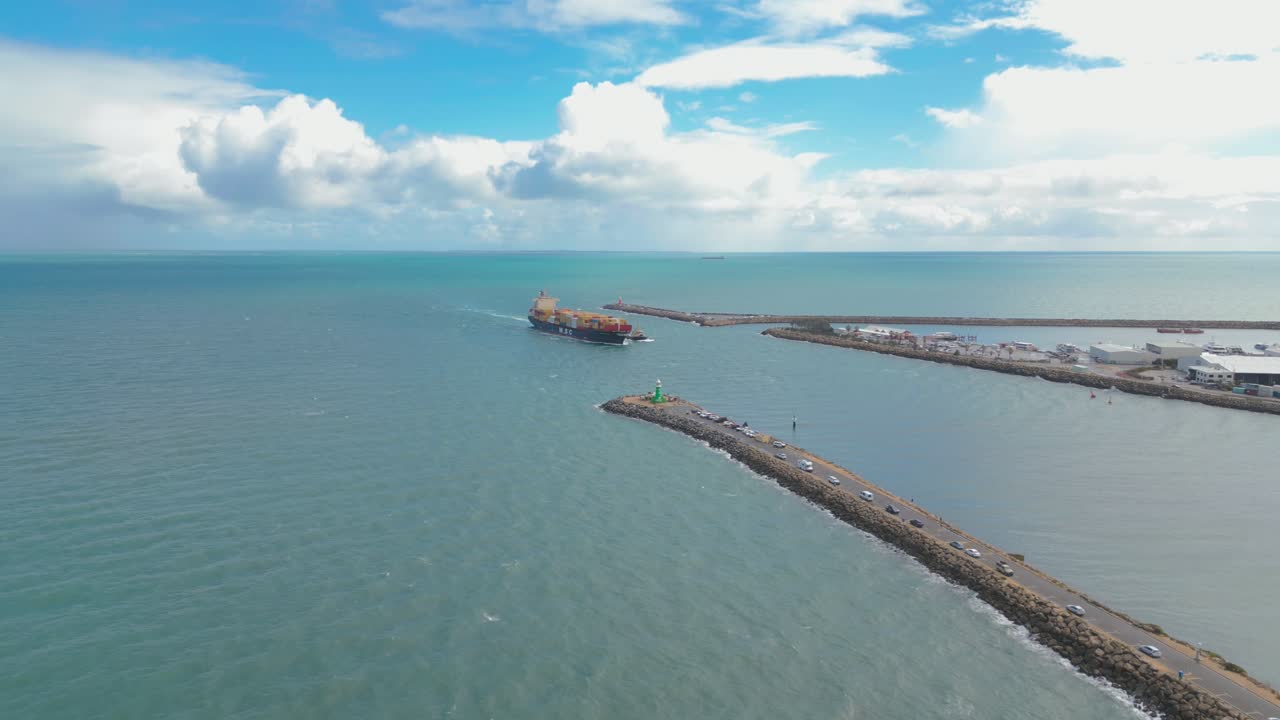 Stunning aerial footage providing a bird's eye view of the South Mole Lighthouse, with a huge cargo ship advancing towards the docks in Fremantle, Perth, Western Australia