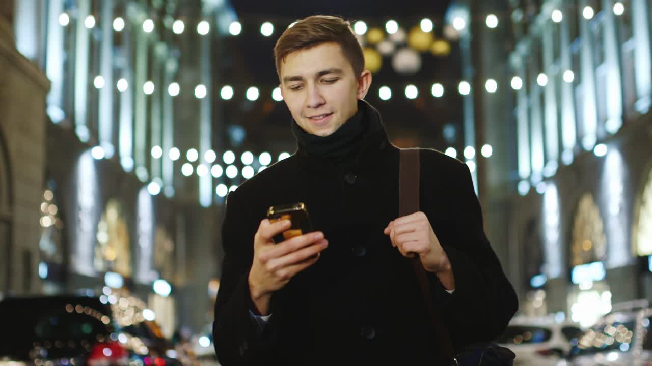 젊은 남자가 밤의 도시를 걷고 스마트폰을 사용 2