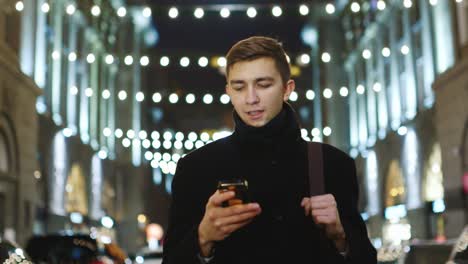 A-young-man-walks-through-the-night-city-and-uses-a-smartphone-2