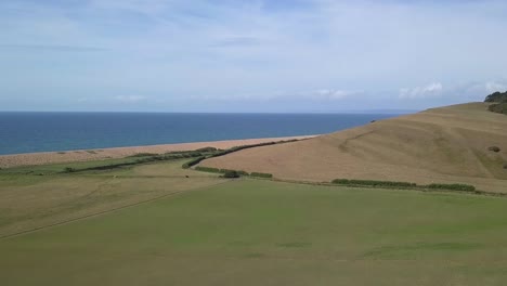 low forward tracking aerial moving upwards over a field revealing the vast expanse of the dorset coastline at the west end of chesil beach