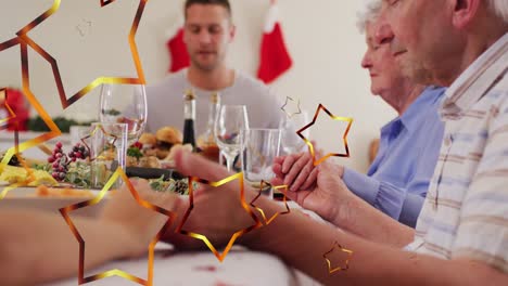 animación de estrellas sobre familia caucásica con sombreros de santa orando antes de la cena de navidad.