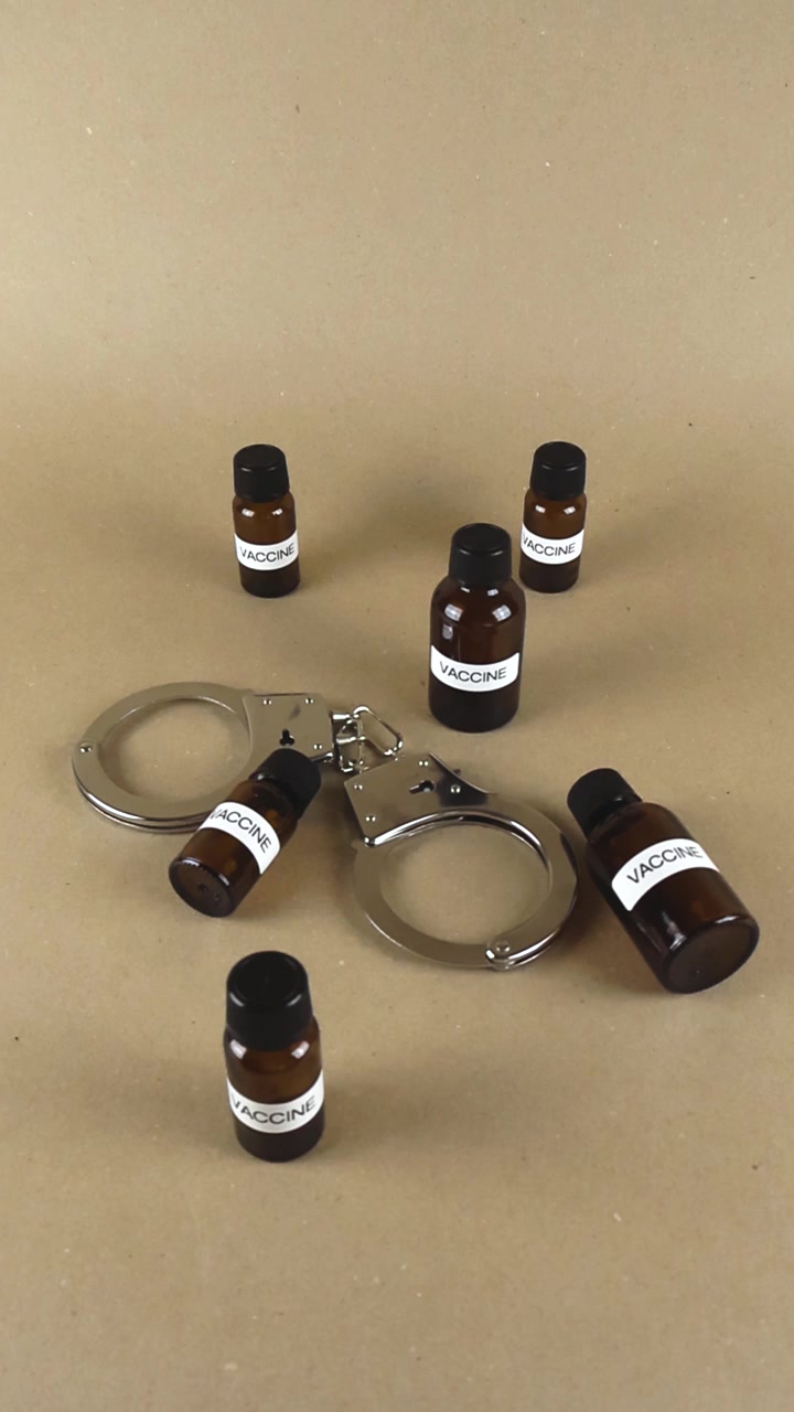 Flaconi di vaccino con etichette e manette in metallo su una superficie marrone che suggeriscono l'immunizzazione forzata, le politiche di vaccinazione obbligatoria o le controversie sulla libertà medica contro le leggi governative