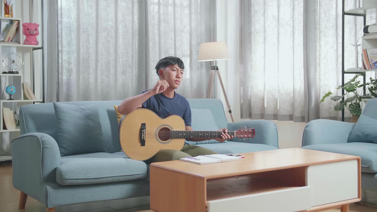 집에서 종이에 음악을 작곡하기 전에 기타를 들고 있는 아시아 소년 작곡가