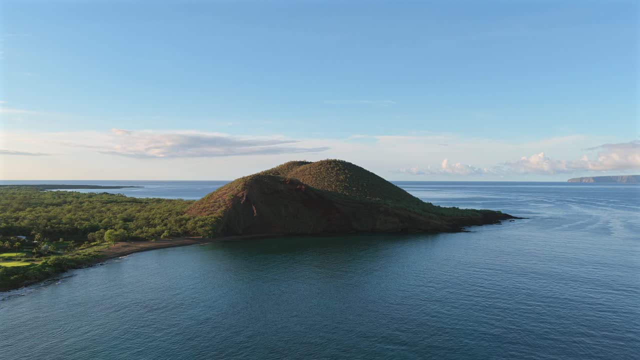 Smooth drone ascent over a dramatic volcanic coastal headland, revealing turquoise tropical water under soft morning light. Ideal for travel, nature, and cinematic establishing scenes