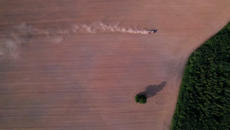 vista general estática aérea de arriba hacia abajo del tractor que conduce a través de un campo seco y polvoriento