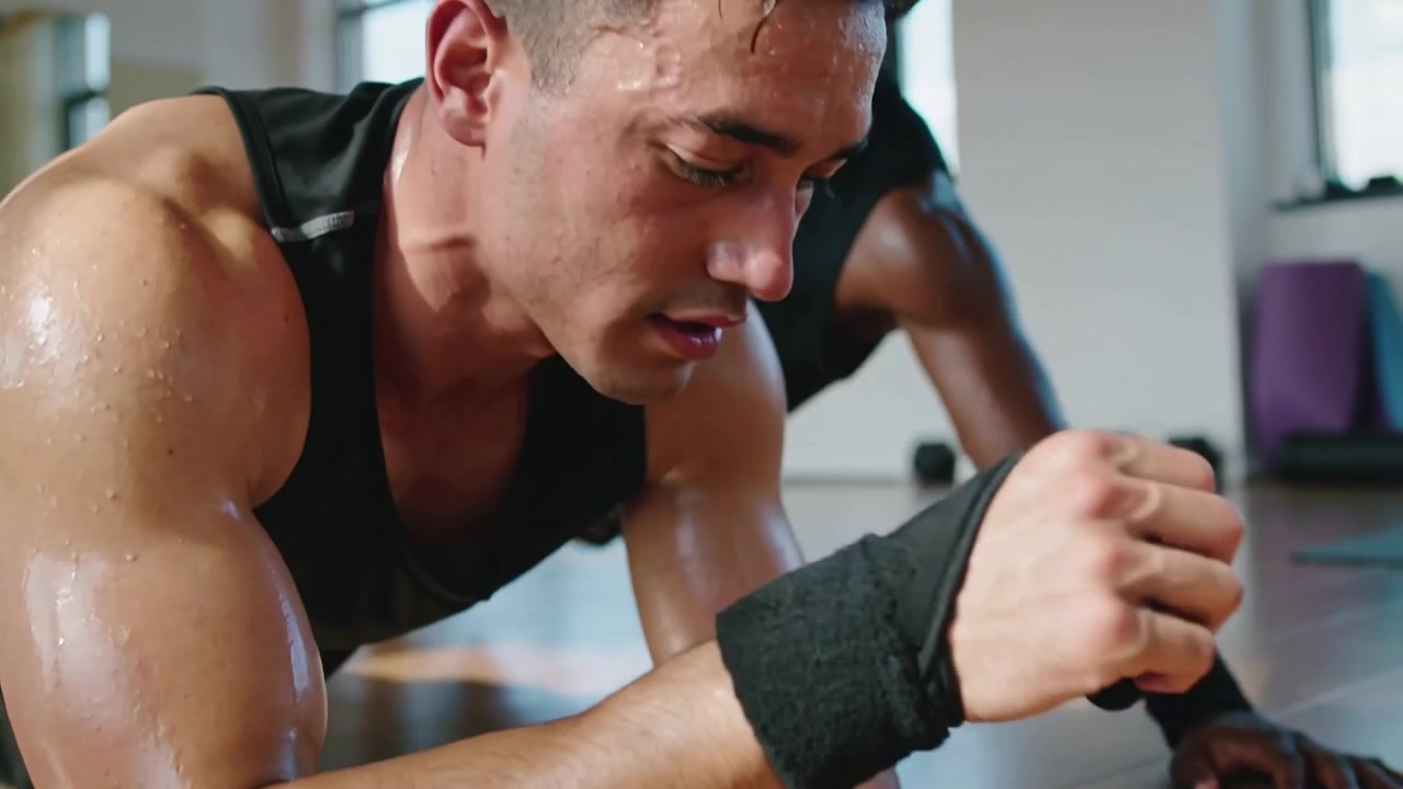 Holding plank, man in black tank at gym on cue, building core strength, wearing wrist wraps