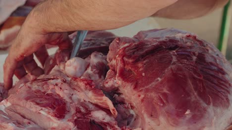 detailed close up of a butcher carving raw pork shoulder during traditional meat processing
