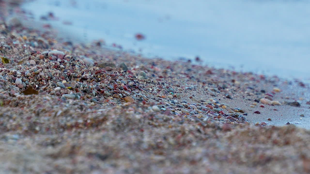 부드러운 초점 작은 파도가 초점을 맞추지 않은 자갈 모양의 해변을 가까이에서 볼 수 있습니다.