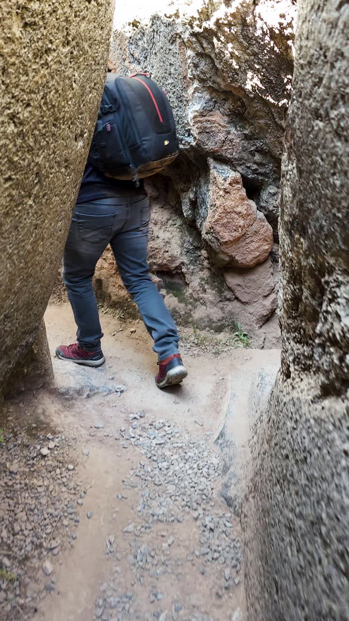 A young man walks through the ancient stone pathways of the Qenqo archaeological complex in Cusco, Peru. The footage captures the historic atmosphere and impressive stonework of the Inca ruins
