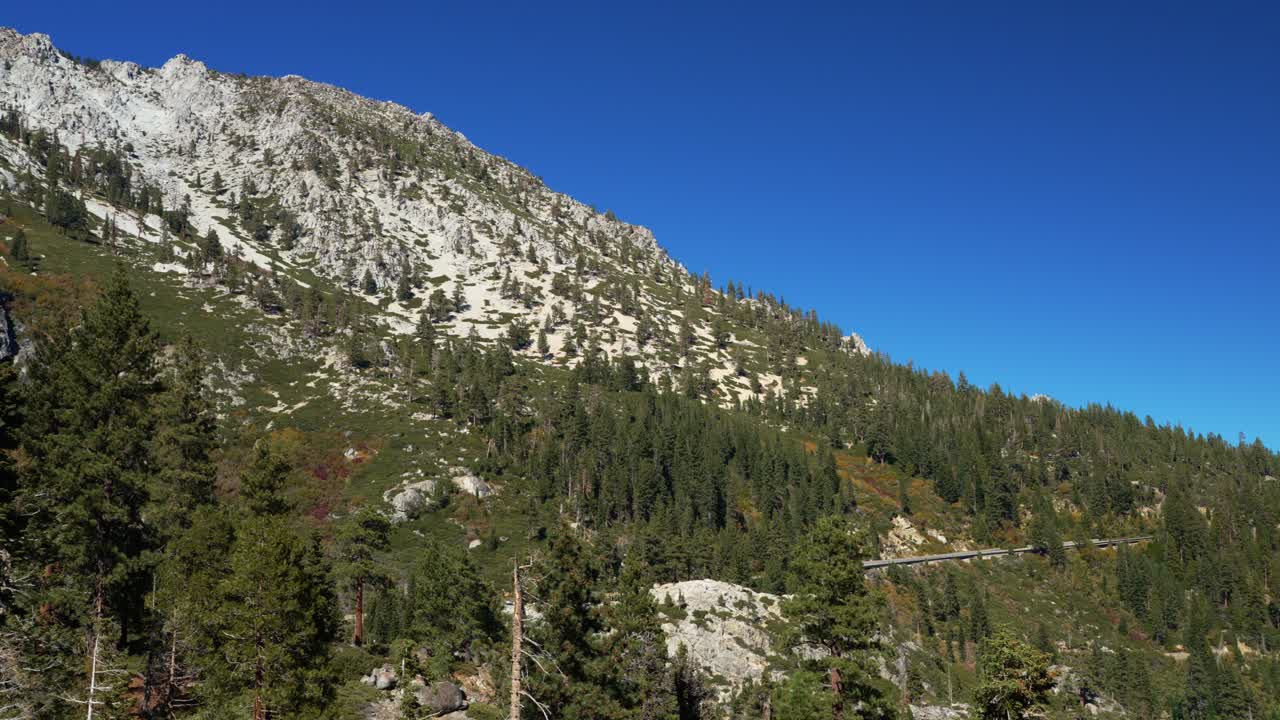 Versante montuoso di granito con pineta sotto un cielo azzurro limpido.